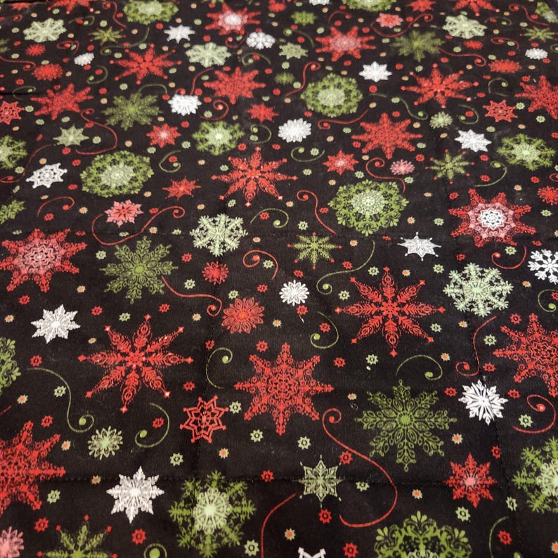 May include: A black fabric featuring a repeating pattern of snowflakes in shades of red, lime green, and white. The design includes intricate, varied snowflake shapes interspersed with small dots and thin, curved lines across the surface.