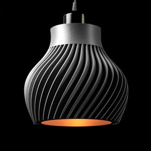 Op de afbeelding: Een moderne hanglamp met een zilverkleurige bovenkant en een spiraalvormig, geribbeld ontwerp in grijstinten. De onderkant van de lamp heeft een warme, oranje gloed, die contrasteert met de donkere achtergrond. Deze eigentijdse lamp is ontworpen voor gebruik binnenshuis.