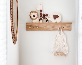 May include: A wooden shelf with three wooden animal figurines: a lion, a giraffe, and an elephant. The shelf has five hooks and a white mesh bag hanging from one of the hooks.
