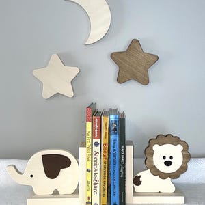 May include: Wooden bookends shaped like an elephant and a lion, with a brown and white color scheme. The bookends are holding up a stack of children's books with titles like "Stories to Share" and "Biscuit Storybook Favorites".