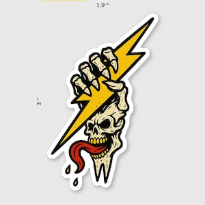 May include: A sticker depicting a skull with a yellow lightning bolt held in a skeletal hand. The skull has a red tongue and is dripping. The sticker is approximately 7.6 cm tall and 4.8 cm wide.