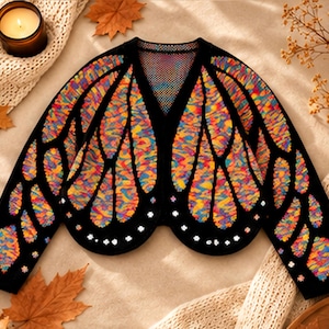 May include: A black long-sleeve cardigan featuring a vibrant, multi-coloured butterfly wing pattern in shades of orange, yellow, blue, and purple. The garment has a V-neckline and is decorated with small, white, flower-shaped embellishments.