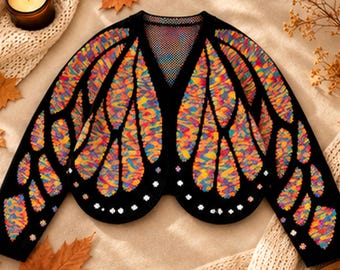 Op de afbeelding: Een zwart vest met lange mouwen en een levendig, meerkleurig vlindervleugelpatroon in tinten oranje, geel, blauw en paars. Het kledingstuk heeft een V-hals en is versierd met kleine, witte, bloemvormige decoraties.