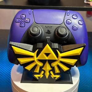 May include: A purple video game controller with a black and yellow Triforce stand. The controller has a PlayStation logo on the front.