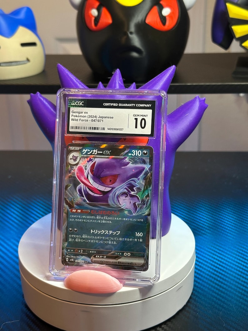 May include: A graded Pokemon trading card featuring Gengar ex from the Wild Force set. The card is in Gem Mint condition and has a grade of 10. The card is in a clear plastic case with a white label that says "Certified Guaranty Company".