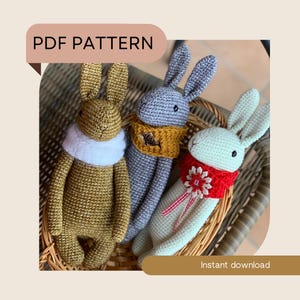 May include: PDF pattern for crocheting three bunny amigurumi toys. The bunnies are in a wicker basket and are wearing different colored scarves. The bunnies are gold, gray, and white.