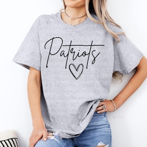 Könnte beinhalten: Ein hellgraues T-Shirt mit dem Wort "Patriots" in schwarzer Schrift und einem Herzsymbol darunter. Das Shirt ist ein kurzärmeliges Rundhals-T-Shirt.