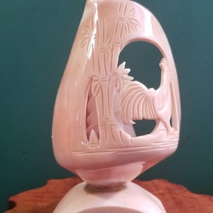 May include: A hand-carved shell sculpture of a rooster standing in front of bamboo. The sculpture is a light pink color and is mounted on a base.