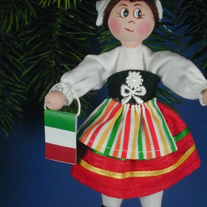 May include: A handmade Christmas ornament depicting a girl wearing a traditional Italian dress with a red, white, and green striped skirt and a green, white, and red flag.