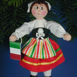 May include: A handmade wooden doll ornament dressed in a traditional Italian costume. The doll is wearing a white blouse, a green and red striped skirt, and a red apron. The doll is holding a small Italian flag.