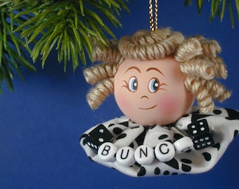 May include: A handmade Christmas ornament featuring a doll with blonde yarn hair, a white and black polka dot dress, and the word "BUNC" spelled out with black and white dice.