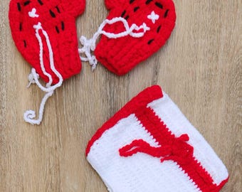 May include: Handmade crochet set in red and white. The set includes two heart-shaped pieces with black and white accents, connected by white yarn, and a square piece with red trim and a red design.