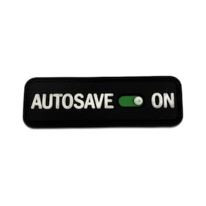 May include: A black rectangular patch with the words "AUTOSAVE ON" in white block letters. A green slider indicates the "ON" position. The patch has a textured appearance.