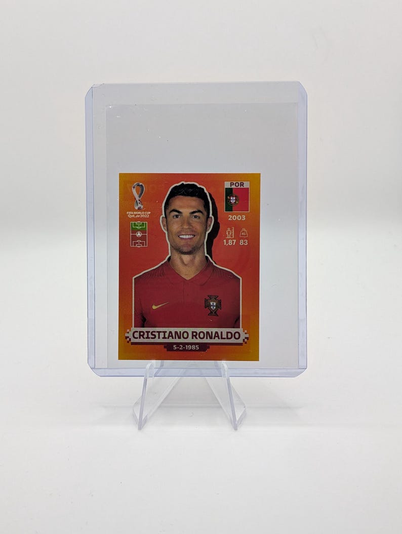 May include: A Cristiano Ronaldo trading card in a protective sleeve. The card features a portrait of Ronaldo in a red jersey, with the text "CRISTIANO RONALDO" and the date "5-2-1985". The card also includes the Portuguese flag and other details.