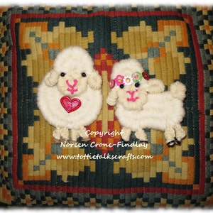 May include: Two fluffy, cream-colored sheep appliqués with pink facial features and black eyes are displayed on a patterned pillow. One sheep has a red heart, the other a floral crown. The pillow has a geometric design.