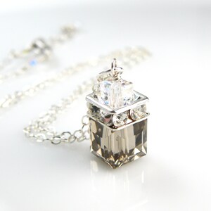 May include: A silver chain necklace with a clear crystal pendant. The pendant is a square shape with smaller crystals around the edges.