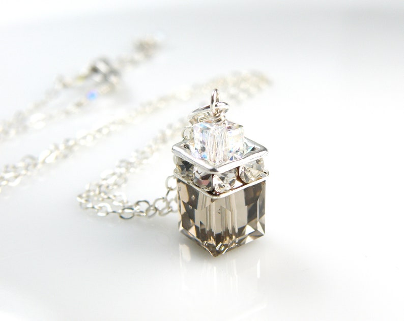 May include: A silver chain necklace with a clear crystal pendant. The pendant is a square shape with smaller crystals around the edges.