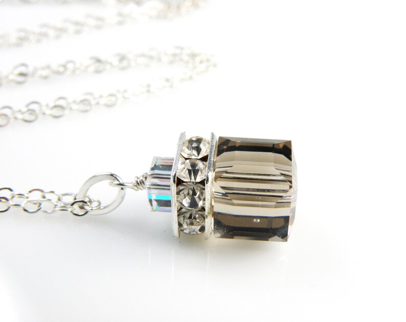 May include: A silver chain necklace with a pendant featuring a faceted smoky quartz stone surrounded by clear rhinestones.