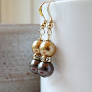 May include: Gold and black pearl dangle earrings with a crystal accent. The earrings have a simple design and are perfect for everyday wear.