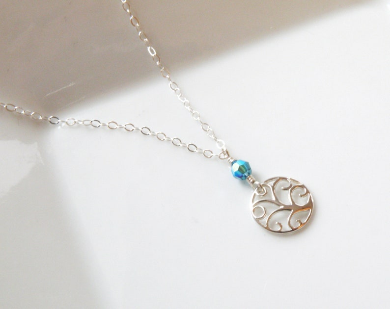 Puede incluir: Un delicado collar de plata con un colgante circular calado y una peque&ntilde;a cuenta azul iridiscente. La fina cadena es elegante. El colgante presenta un dise&ntilde;o decorativo con volutas.