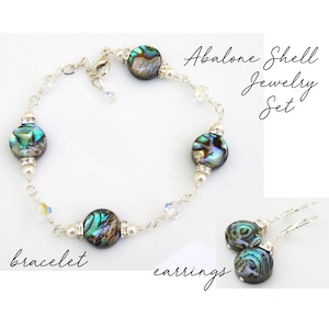 Puede incluir: Conjunto de joyas de concha de abulón con un brazalete de cadena de plata y pendientes a juego. El brazalete tiene cuatro cuentas de concha de abulón y detalles de cristal. Los pendientes son de plata con gotas de concha de abulón.