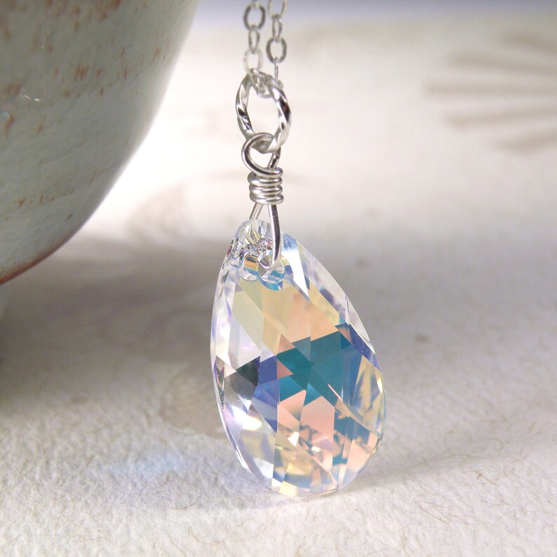 Pu&ograve; includere: Una collana con catena d'argento con un ciondolo di cristallo iridescente a forma di lacrima.