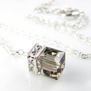 May include: A silver chain necklace with a clear, faceted, gray crystal pendant. The pendant is set in a silver frame with smaller clear crystals.