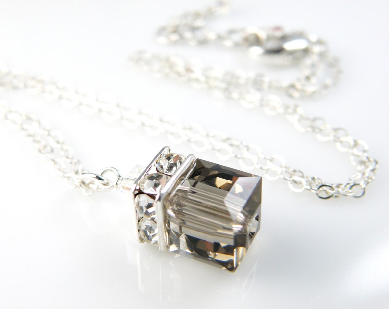 May include: A silver chain necklace with a clear, faceted, gray crystal pendant. The pendant is set in a silver frame with smaller clear crystals.