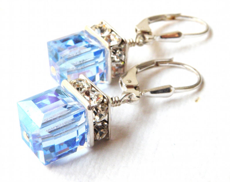 crystal cube dangle earrings in light sapphire blue color with silver rhinestone crowns on top and set on silver leverback earring closures