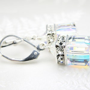 Puede incluir: Pendientes de aro de plata con un cubo de cristal transparente iridiscente y un adorno de cristal plateado.