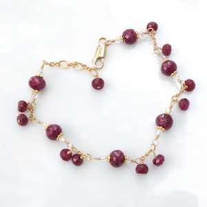 May include: A gold chain bracelet with red gemstone beads and clear crystal accents.