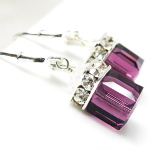 May include: Silver dangle earrings with a purple crystal and clear rhinestones.