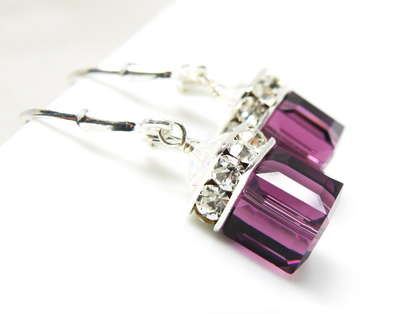 May include: Silver dangle earrings with a purple crystal and clear rhinestones.