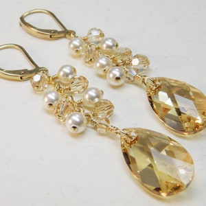 May include: Gold dangle earrings with a teardrop-shaped crystal and a cluster of pearls and clear crystals.