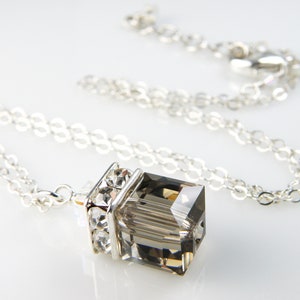 May include: A silver chain necklace with a clear, faceted, rectangular pendant. The pendant is set in a silver frame with clear crystals.