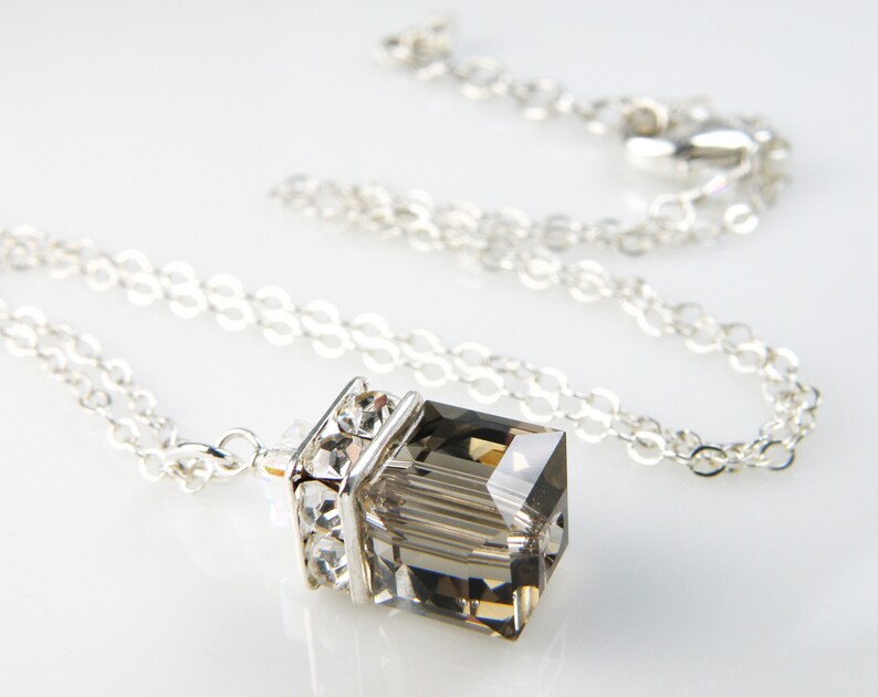 May include: A silver chain necklace with a clear, faceted, rectangular pendant. The pendant is set in a silver frame with clear crystals.