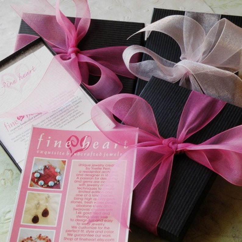 Puede incluir: Cajas de regalo negras atadas con cintas rosas y blancas transparentes. Las cajas est&aacute;n dispuestas con una tarjeta que dice "fine heart exquisita joyer&iacute;a artesanal". La tarjeta tiene im&aacute;genes de joyas y texto.