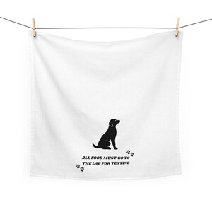 May include: White kitchen towel with a black silhouette of a dog and paw prints. Text reads "ALL FOOD MUST GO TO THE LAB FOR TESTING". The towel is hanging from a clothesline with wooden clothespins.