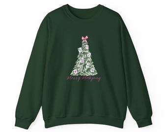 May include: A dark forest green crewneck sweatshirt featuring a graphic of a Christmas tree decorated with mahjong tiles and a pink bow at the top. The text Merry Mahjong is printed in pink cursive script below the tree illustration.
