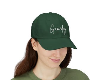 Könnte beinhalten: Dunkelgrüne Baseballkappe mit dem Wort "Gameday" in weißer Schrift. Die Kappe hat einen gebogenen Schirm und ein klassisches Sechs-Panel-Design. Der Hut ist aus einem weichen Material gefertigt und eignet sich für Freizeitkleidung.