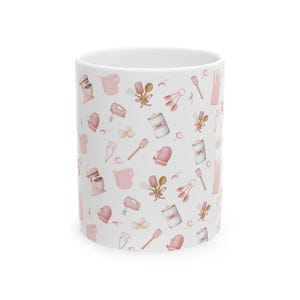 May include: White ceramic mug with a pink and brown pattern of baking tools and ingredients. The pattern includes a mixer, measuring cups, spatulas, whisks, oven mitts, and jars labeled "Sugar".