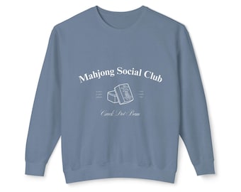 May include: A light blue sweatshirt with the text "Mahjong Social Club" and "Crack Pot Bam" in white. A white outline of a mahjong tile is in the center of the design.