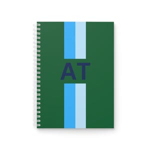 Könnte beinhalten: Ein grünes Notizbuch mit einem blauen und weißen Streifen in der Mitte. Das Notizbuch hat die Buchstaben "AT" in Marineblau auf der Vorderseite.