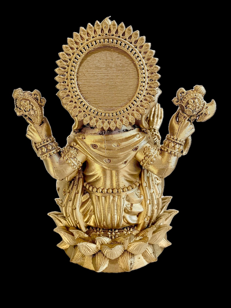 May include: A gold-colored statue of the Hindu goddess Lakshmi, sitting on a lotus flower. She is holding a pot of gold in one hand and a lotus flower in the other. She is wearing a crown and jewelry. The statue is a traditional Indian religious icon.