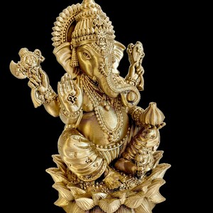 May include: A gold-colored statue of Ganesha, the Hindu god of wisdom and prosperity, sitting on a lotus flower. The statue is intricately detailed with ornate jewelry and a crown.