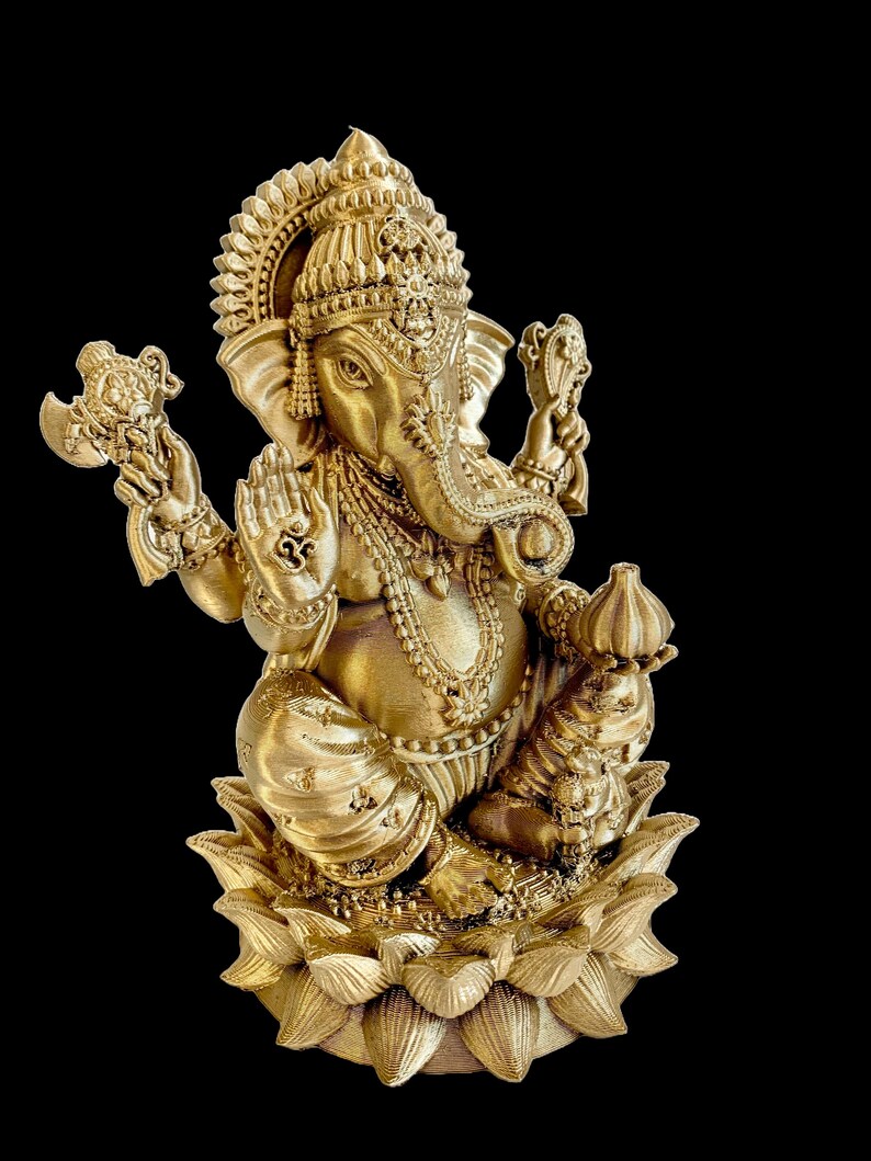 May include: A gold-colored statue of Ganesha, the Hindu god of wisdom and prosperity, sitting on a lotus flower. The statue is intricately detailed with ornate jewelry and a crown.