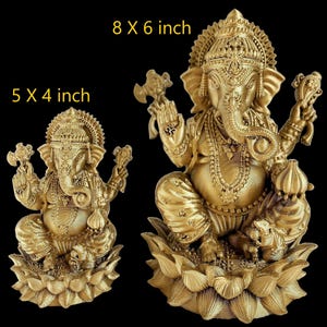 May include: Two gold-colored Ganesha statues, one is 5 x 4 inches and the other is 8 x 6 inches. Both statues are sitting on lotus flower bases.