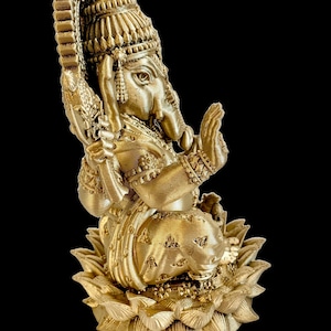 May include: A gold-colored statue of Ganesha, the Hindu god of wisdom and prosperity, sitting on a lotus base. The statue is intricately detailed and features a crown, a trunk, and a small mouse.