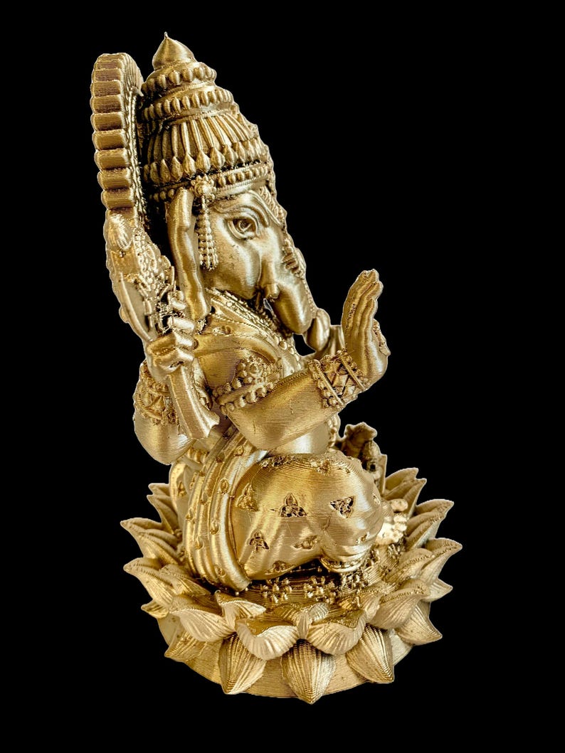 May include: A gold-colored statue of Ganesha, the Hindu god of wisdom and prosperity, sitting on a lotus base. The statue is intricately detailed and features a crown, a trunk, and a small mouse.