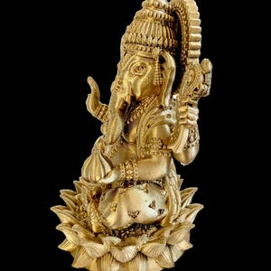 May include: A gold-colored statue of Ganesha, the Hindu god of wisdom and prosperity, sitting on a lotus flower base. The statue is intricately detailed with ornate jewelry and a crown.